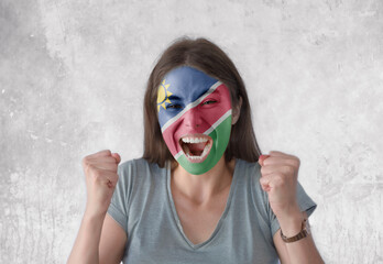 Young woman with painted flag of Namibia and open mouth looking energetic with fists up