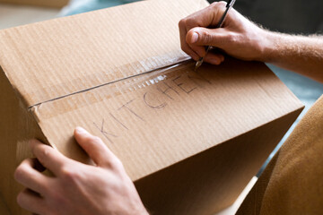 Young man labeling box with kitchen supplies while moving into new home