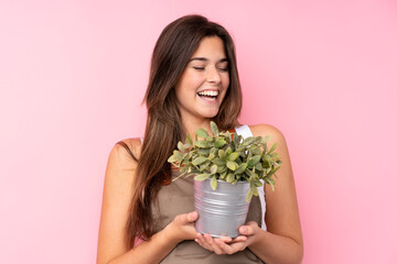 Teenager gardener girl holding a plant over isolated pink background