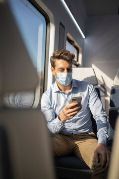 Businessman with protective face mask using mobile phone while sitting in train during COVID-19