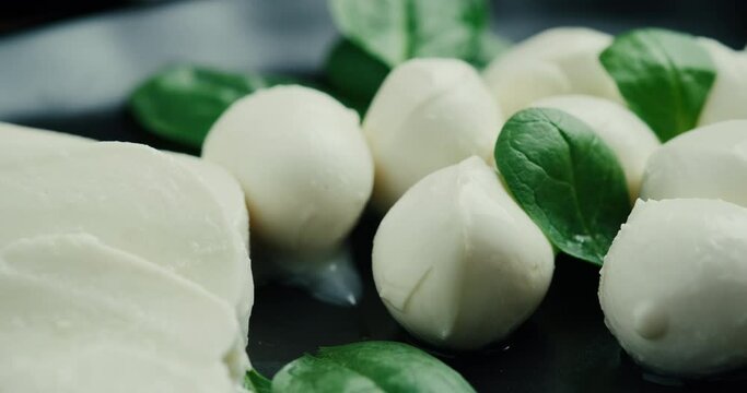 White small mozzarella cheese balls, spinach leaves on black plate. Rotaiting shot.