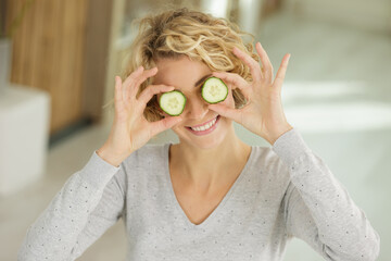 playful young woman standing covering her eyes with cucumber
