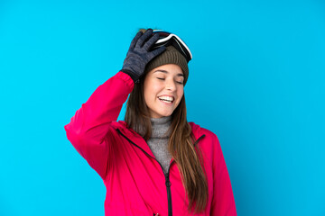 Teenager skier girl with snowboarding glasses over isolated blue background laughing