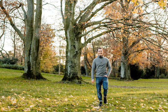 Smiling man walking on grass in front of trees in public park