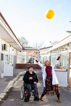 Cheerful female nurse and disabled man playing with ball against sky at rehabilitation center