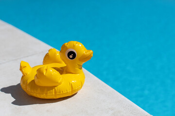 Inflatable yellow mini duck, cocktail stand near swimming pool on bright sunny day, copy space. Concept of summer vacation, entertainment, water, air, sunbathing, health. Side view. Horizontal