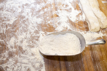 Wheat flour on a wooden table and a measuring spoon.