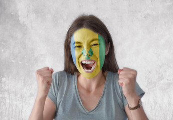 Young woman with painted flag of Saint Vincent and the Grenadines and open mouth looking energetic...