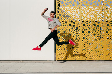 Carefree man with headphones and mobile phone jumping against wall