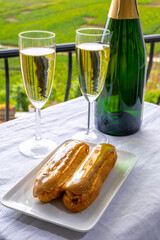 Taste of France, fresh baked eclair cakes with caramel cream with champagne traditional sparkling wine and view on green vineyards of Champagne, France