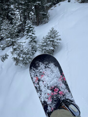 Personal point of view while seated on a chair lift, looking down at a snowboard and snow covered...