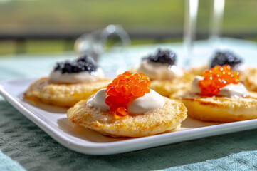 Tasting and pairing of french champagne wine with pancakes, creme fresh, red and black fish caviar and view on green vineyards of Champagne near Epernay on background