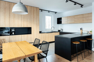 Luxurious kitchen in apartment with kitchen island, granite counter and woooden cupboard and floor. Exclusive space with stylish chairs and furniture. Bright home.