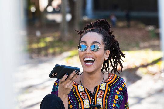 Cheerful fashionable young beautiful woman talking on mobile phone while sitting at park