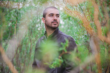 attractive man in a leather jacket is walking through the jungle
