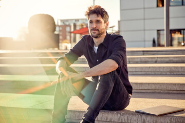 Thoughtful businessman sitting by laptop on steps