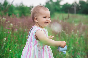 beautiful baby in a striped dress watering flowers in the garden