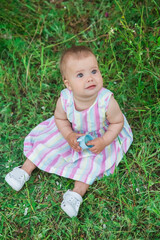 beautiful baby in a striped multi-colored dress sitting in a field on the grass