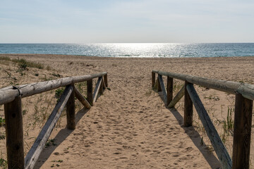 wooden boardwalk and beach access leads directly onto beach with glistening calm ocean behind