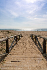wooden boardwalk and beach access leads directly onto beach with glistening calm ocean behind