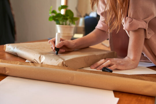 Female freelancer writing message on wrapped package at desk in living room