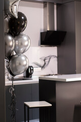 Corner of stylish Minimalistic grey kitchen, dark gray cupboards, white countertops and bar with stools. black and white balloons.