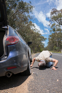 Man changes a tyre after getting a flat tyre on a country road
