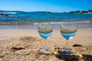 Fototapeta na wymiar Two glasses of local dry white wine on white sandy beach and blue Mediterranean sea on background, near Le Lavandou, Provence, France