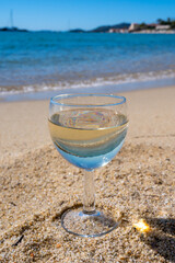 Glass of local dry white wine on white sandy beach and blue Mediterranean sea on background, near Le Lavandou, Provence, France