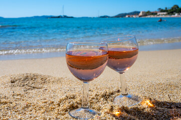 Two glasses of local rose wine on white sandy beach and blue Mediterranean sea on background, near Le Lavandou, Provence, France