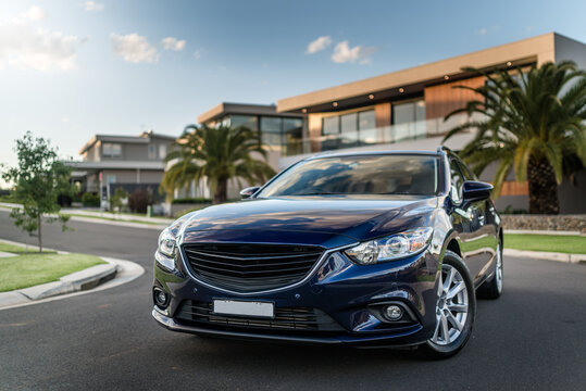 Fototapeta Blue station wagon on suburban street with luxury homes