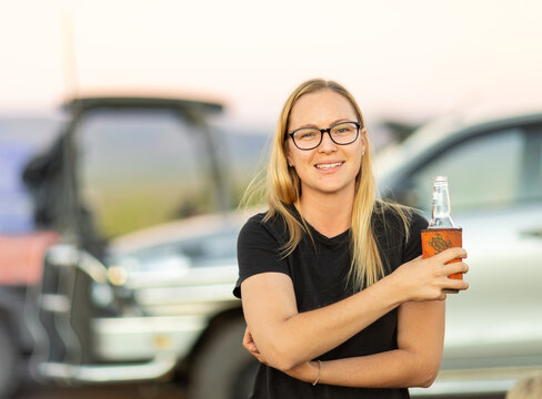 blonde bespectacled young woman outdoors holding beer bottle