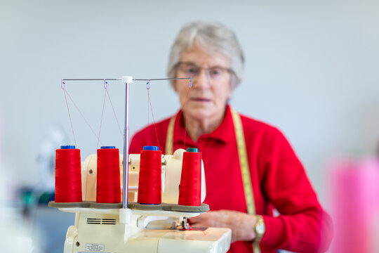 focus on red thread with elderly lady blurred behind sewing machine