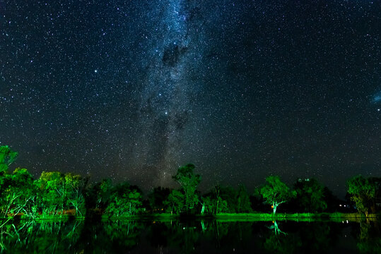 Starry night sky with Milky Way and reflections of trees in a lagoon