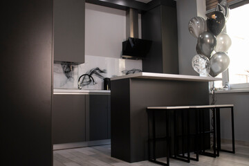 Corner of stylish Minimalistic grey kitchen, dark gray cupboards, white countertops and bar with stools. black and white balloons.