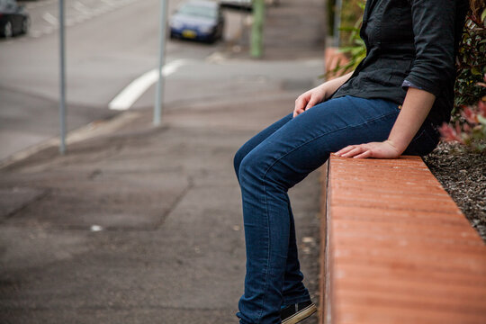 Teen girl sitting on a streetside brick wall