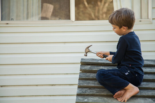 Aussie child hammering nails into roof of outside cubby house