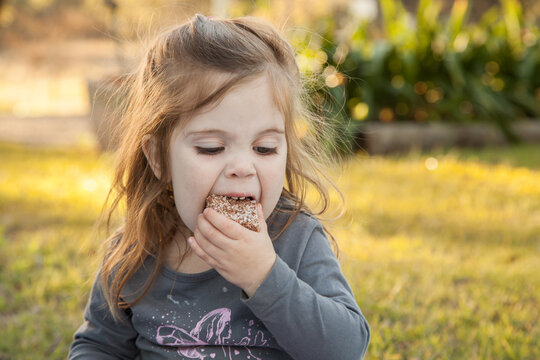 Little Girl Sitting Outside Eating A Lamington