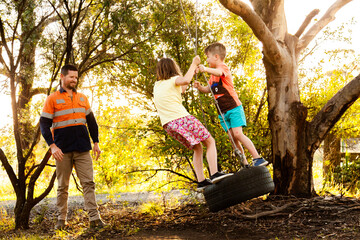 Dad playing with children in backyard on tyre swing in the afternoon