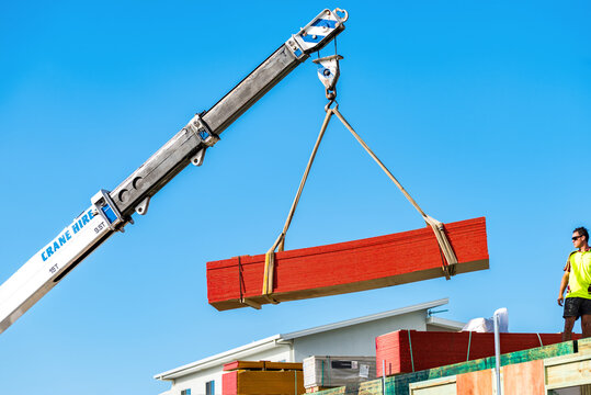 Building material being lifted by a crane to the second level with man observing