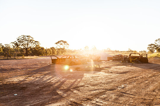 Smashed up burnt out cars on gravel patch backlit by sunflare