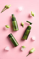 Green cosmetic containers, flowers, ice cubes on pink background. Natural beauty products concept.