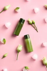 Green cosmetics packaging with ice cubes and frozen flowers on pink background. Natural beauty SPA products concept.