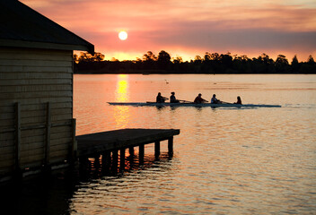 People rowing past a jetty on a lake at sunset
