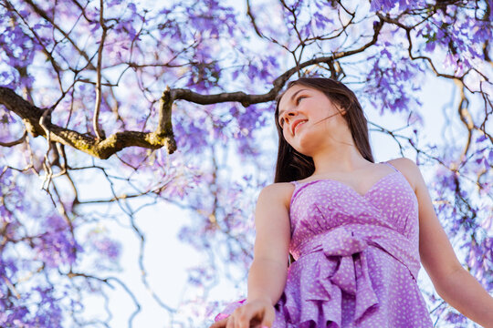 Portrait of a smiling teen girl sitting in a jacaranda tree wearing a purple dress in summer