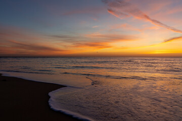 Obraz premium gorgeous colorful sunset over the ocean and beach with gentle waves lapping at the shore
