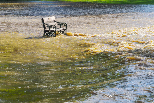 A park bench sits in rushing flood waters