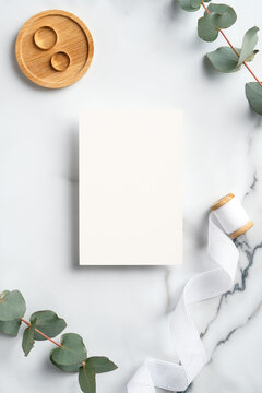 Wedding invite mockup, golden rings, eucalyptus leaves on marble table. Flat lay, top view, copy space.