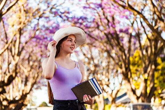 Young teen girl walking down street with hat and books under her arm