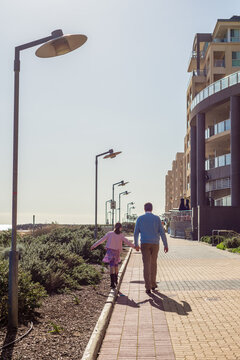 a father holding his daughter's hand as she walks along a coastal path